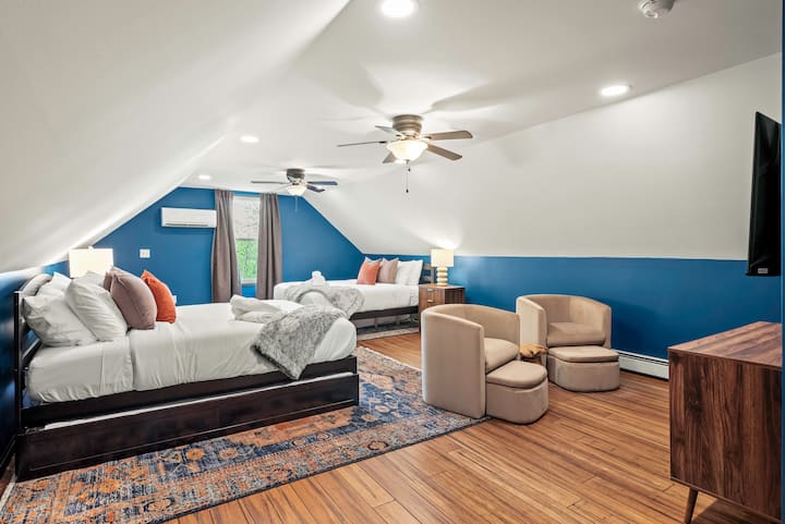 Amplio dormitorio estilo loft en Long Pond, Pensilvania, con dos acogedoras camas tamaño queen, dos camas individuales XL, una vibrante pared decorativa, suelos de madera, una moderna zona de estar y un minisplit personal para mayor comodidad durante todo el año, perfecto para relajarse con familiares o amigos.
