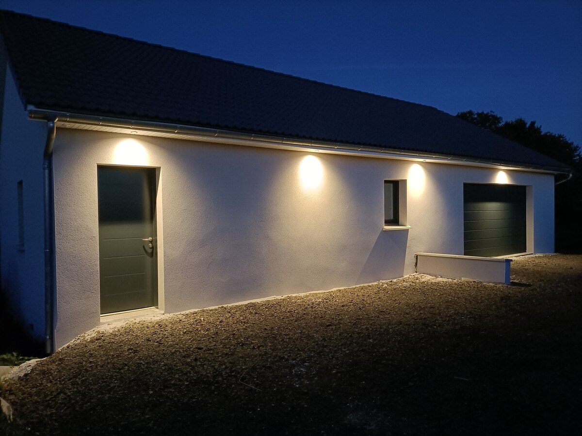 A modern exterior of a newly constructed building is illuminated by soft lighting at dusk. Two doors are visible, alongside a window, emphasizing the clean lines and fresh design of the property, set against a gravel path.