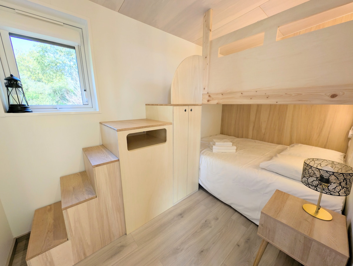 Cette photo montre l'ingénieux lit superposé. Un escalier en bois mène au couchage supérieur, et ses marches servent aussi de rangements intégrés. Le lit du bas, éclairé, est prêt à vous accueillir.
Draps et serviettes disponibles à la location.