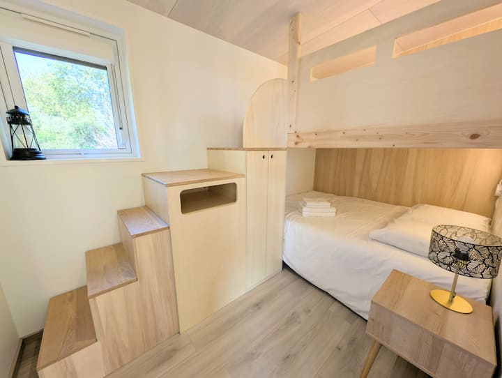 Cette photo montre l'ingénieux lit superposé. Un escalier en bois mène au couchage supérieur, et ses marches servent aussi de rangements intégrés. Le lit du bas, éclairé, est prêt à vous accueillir.
Draps et serviettes disponibles à la location.