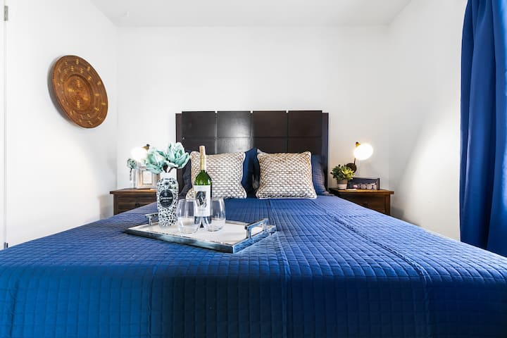 - Dormitorio tamaño king con lujosa ropa de cama azul y mesitas de noche - Iluminación suave, detalles costeros y ambiente sereno - Cómodo refugio en un elegante condominio frente al agua