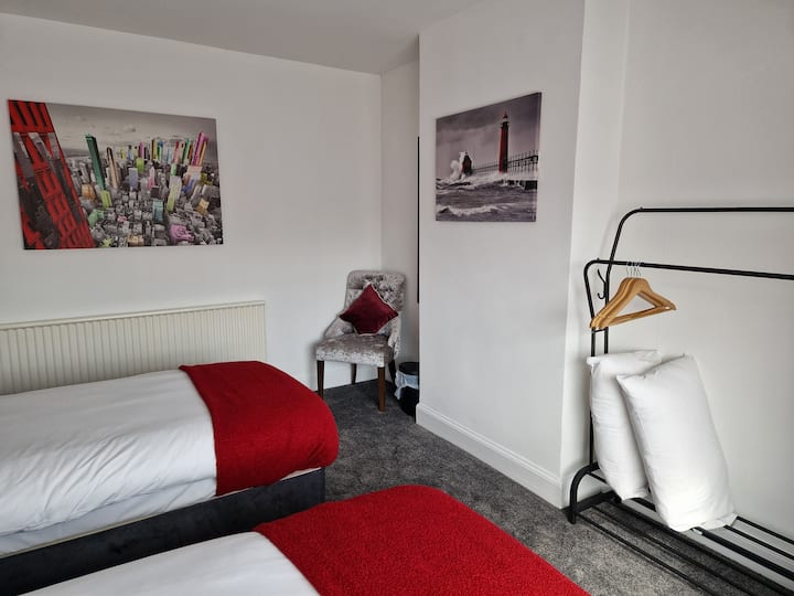 חדר שינה זוגי מסוגנן עם גוונים אדומים בולטים, יצירות אמנות עכשוויות, פינת קריאה נעימה וחלל תלייה פתוח לגישה קלה ונוחה.