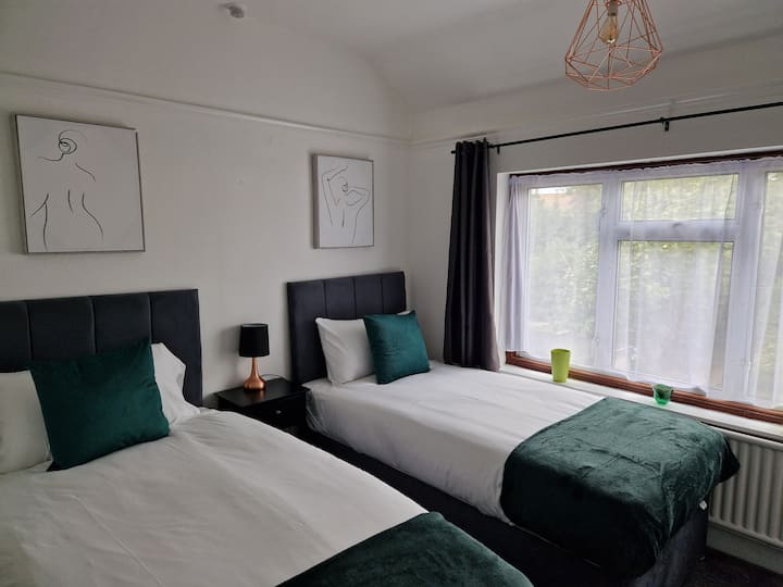 חדר שינה זוגי שיקי עם ראשי מיטה שחורים עכשוויים, גימורים מינימליסטיים עדינים ואור טבעי חם הזורם דרך החלון.