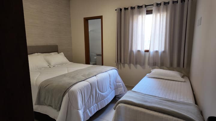 Habitación suite con una cama tamaño queen y una cama doble, todas con ropa de cama.