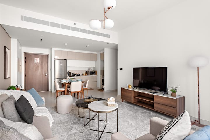 Пространа дневна соба со голем кауч на спуштање, стилска централна масичка за кафе, удобна фотелја и 65-инчен телевизор за забава. Со поглед на трпезаријата и кујничката. 