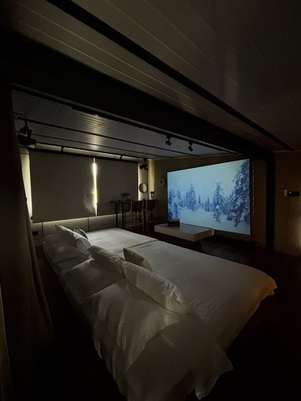 Opción A, 2 camas tatami tamaño king, capacidad para 4 personas cómodamente. Una pantalla de proyector retráctil plateada.