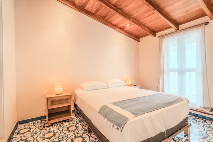 Спокојно засолниште: брачен кревет (широк 150-179 см), амбиентално светло на ноќните масички, дрвен таван и хидрауличен мозаик. Арена со меки текстури и тонови за одмор.