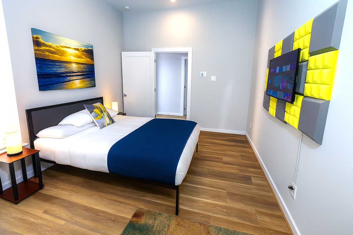 Rustig en modern
Deze kamer biedt een rustig toevluchtsoord met fris wit beddengoed, een marineblauwe plaid en warme houten vloeren. Een muurschildering met zonsondergang en een gemonteerde tv voegen charme en entertainment toe, terwijl zachte verlichting een gezellige, moderne sfeer creëert.
