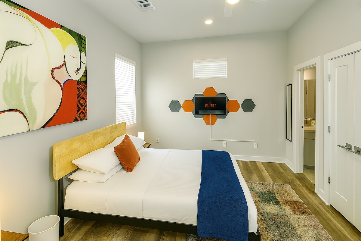 Deze stijlvolle kamer heeft een pluche bed met frisse, witte lakens, opvallende sierkussens en een marineblauwe plaid. Een tv staat op een stralende geometrische achtergrond, perfect om te ontspannen in een ruimte die comfort combineert met een samengesteld design.