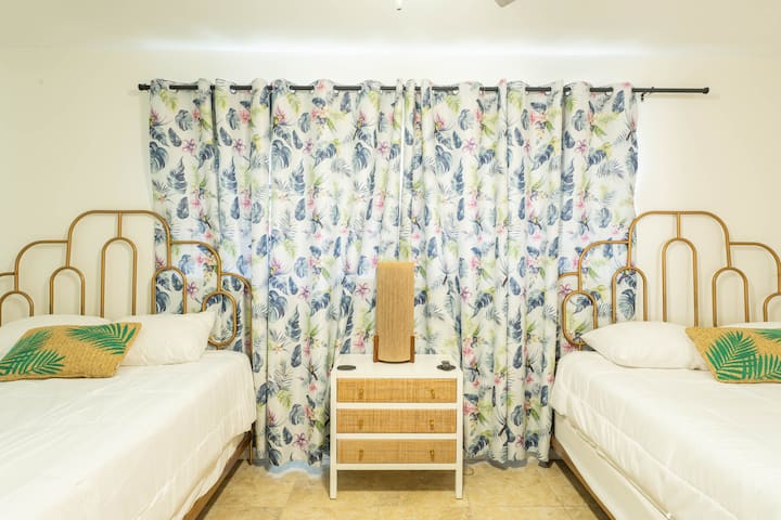Dhomë e ndritshme me dy krevate dopio "queen" dhe perde tropikale për një qëndrim të rehatshëm.