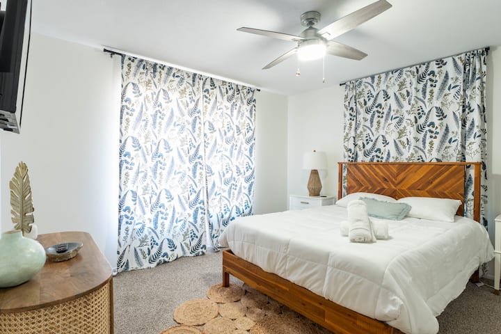 Dhomë gjumi e rehatshme "queen" me perde të modeluara dhe dritë të butë natyrale.