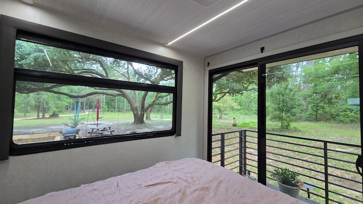 Una cama tamaño queen ubicada bajo el roble, rodeada de ventanas con vistas impresionantes y equipada con persianas opacas para una noche de sueño reparador