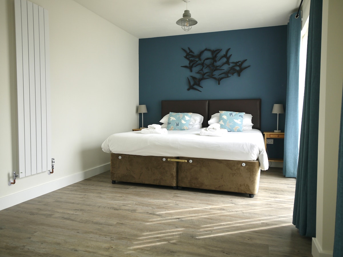 Леглото в тази спалня може да бъде суперголямо двойно легло или две единични легла. Тази снимка показва спалнята, в която е оправено суперголямо двойно легло.