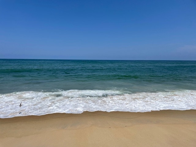 A serene beach scene showcases a smooth stretch of golden sand meeting gentle waves under a clear blue sky. The horizon blends the vibrant blue of the ocean with the lighter tones of the sky, inviting a tranquil atmosphere.