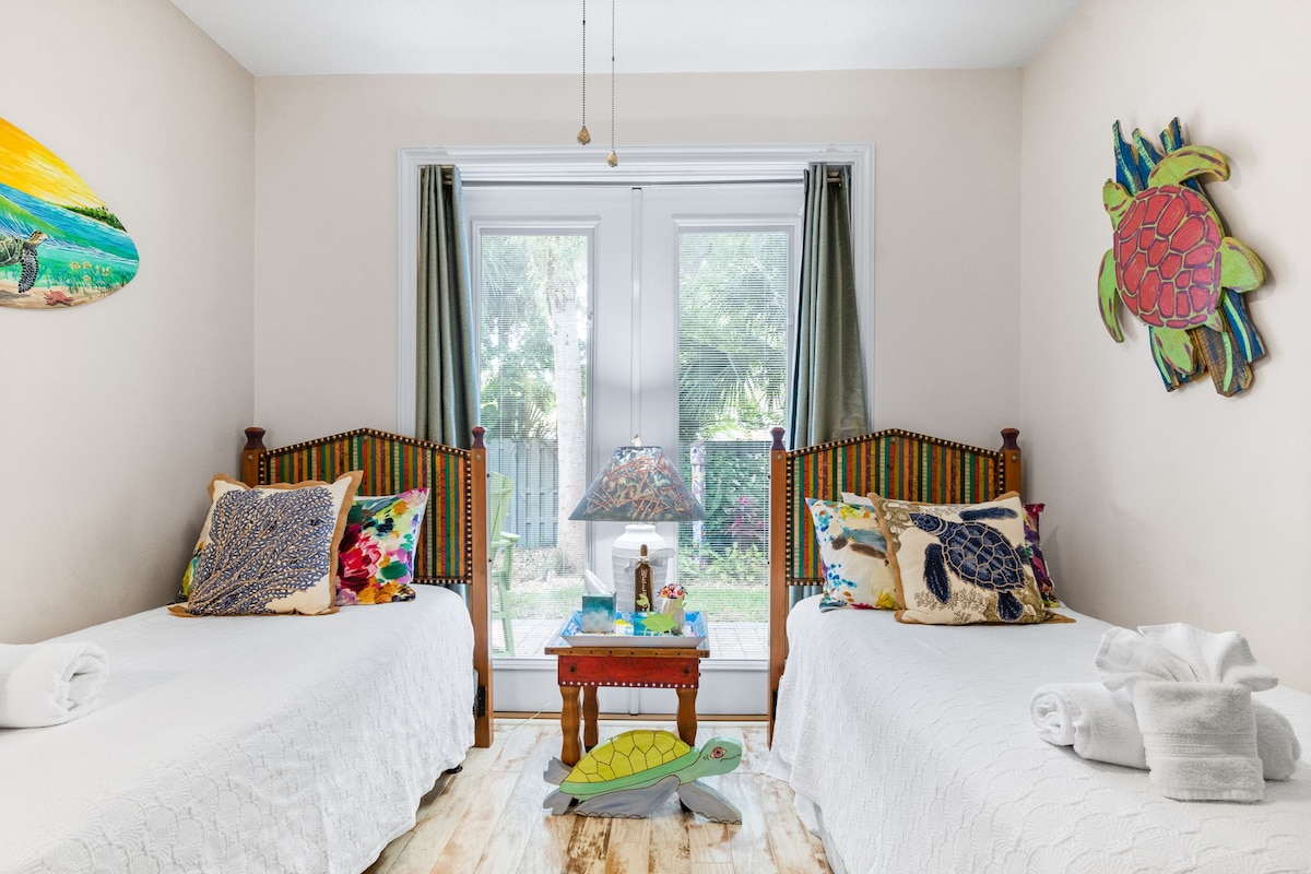 This twin bedroom exudes a cheerful vibe, perfect for a restful stay. It features 2 hand made and hand painted headboards by Shoestring Creations adorned with colorful, tropical-themed pillows. The Sea Turtle theme is carried throughout the house.