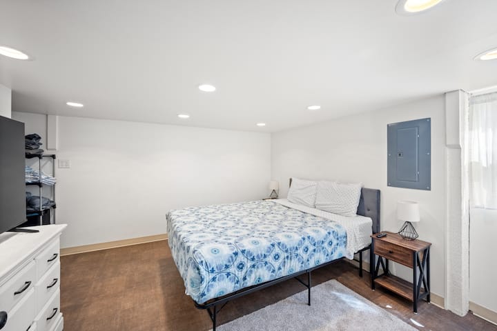 Chumba cha kwanza cha kulala cha malkia katika fleti kina televisheni, dirisha dogo na hifadhi ya mashuka ya ziada.