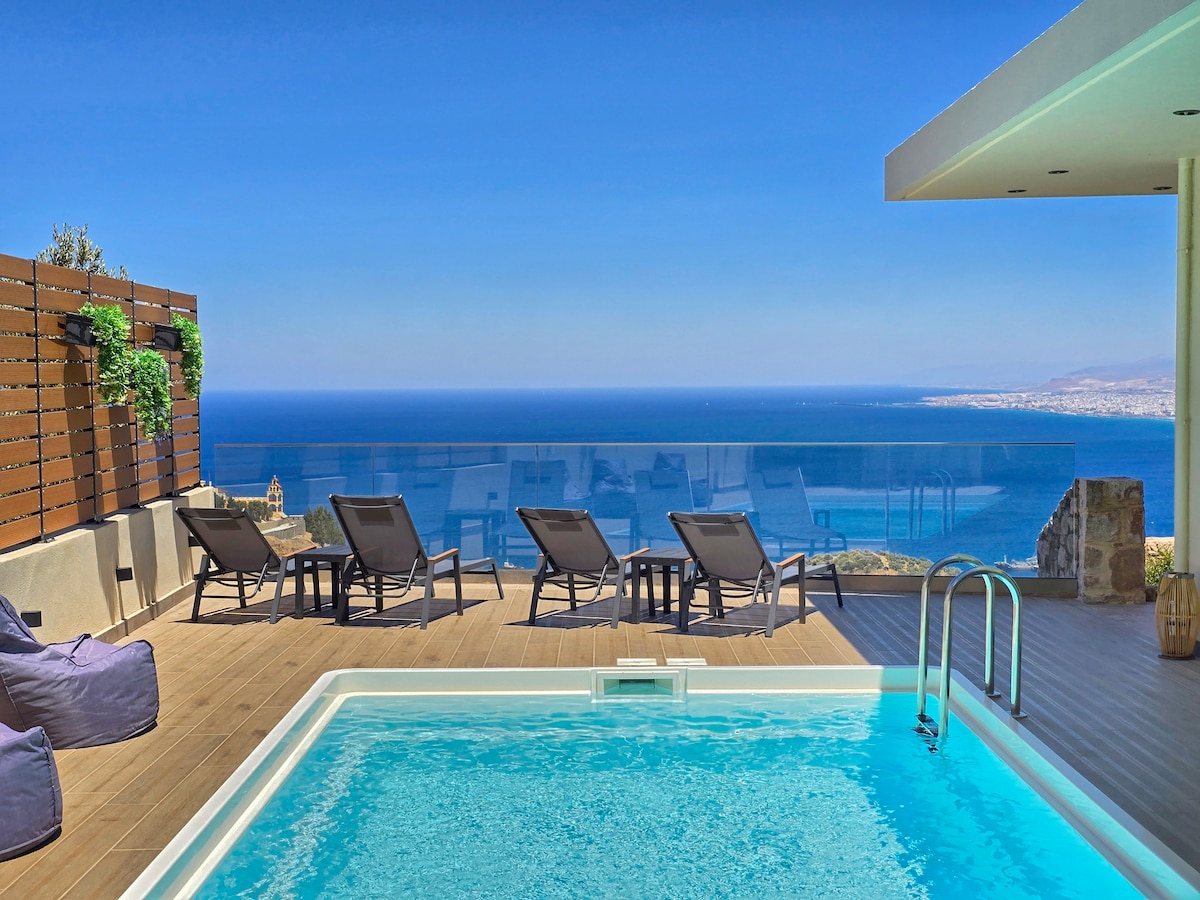 An outdoor area features a private swimming pool with clear waters and six lounge chairs positioned for sunbathing. A panoramic view of the sea and coastline is visible in the background, with a clear blue sky enhancing the tranquil setting.