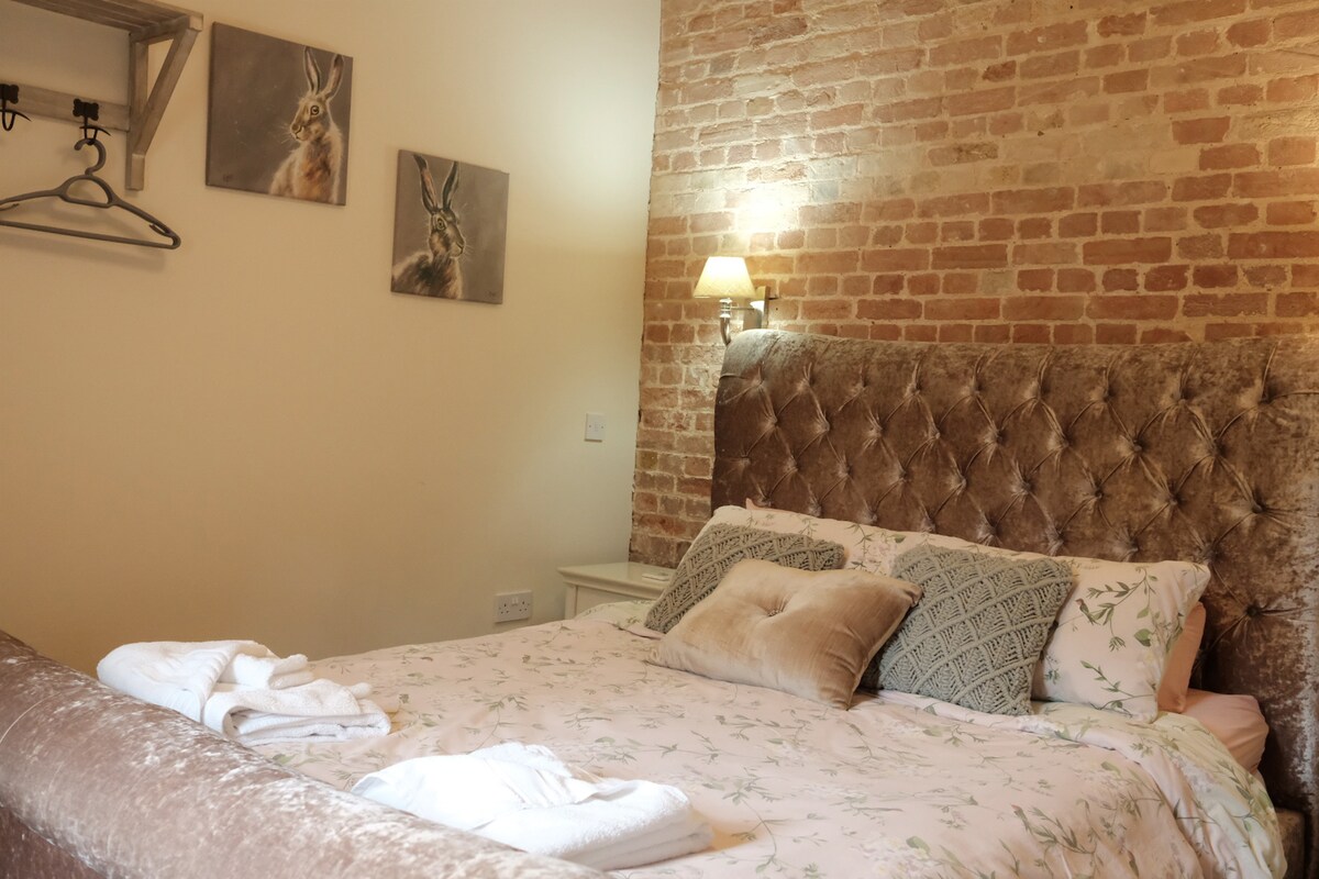 זו מיטת הקינג סייז (חדר שינה 1) בחדר השינה הראשי.  יש גם שידת מגירות, ארונות ליד המיטה ומדף עם ווים למעילים