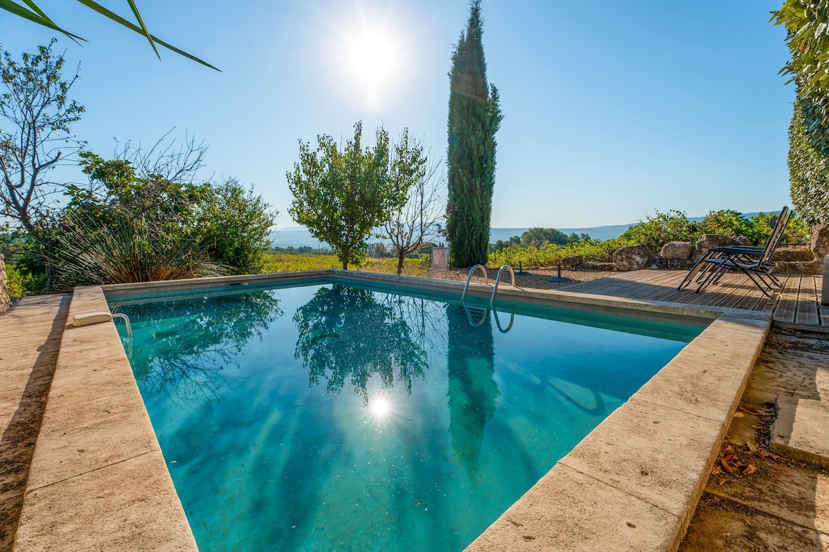 A private swimming pool is set amidst lush greenery, showcasing clear water reflecting sunlight. Surrounding trees add natural beauty, while distant views of the landscape are visible in the background. Sunlight creates a serene atmosphere around the pool area.