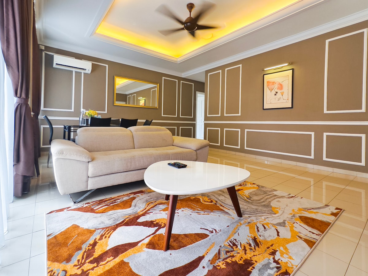 A modern living area features a light-colored sofa, complemented by a patterned area rug with warm tones. A sleek coffee table is positioned centrally. Elegant ceiling details and ambient lighting create a sophisticated atmosphere, while large windows allow natural light to fill the space.