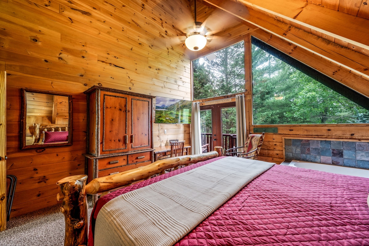 Суит с голямо легло, с прозорец, телевизор и бюро. Истински рустик стил и зелени дървета навън.