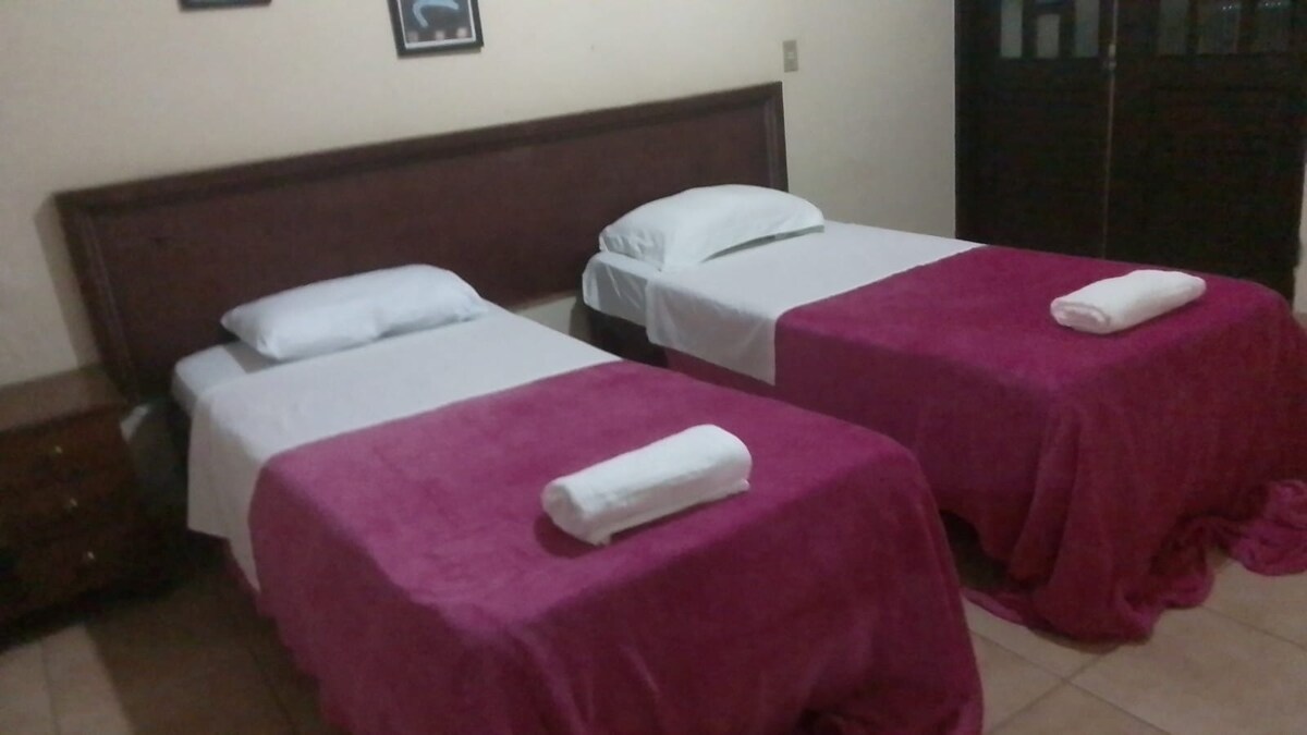 Quarto com sacada equipadp com dois módulos que podem ser configurados como duas camas de solteiro ou uma cama tamanho king.  Ventilador de teto. Conta com amplo salão e banheiro social compartilhado com apenas outro quarto.