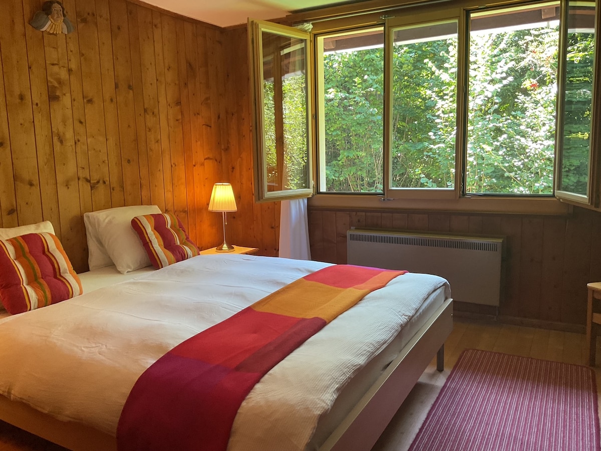 Dormitorio principal con grandes ventanales en el jardín verde.