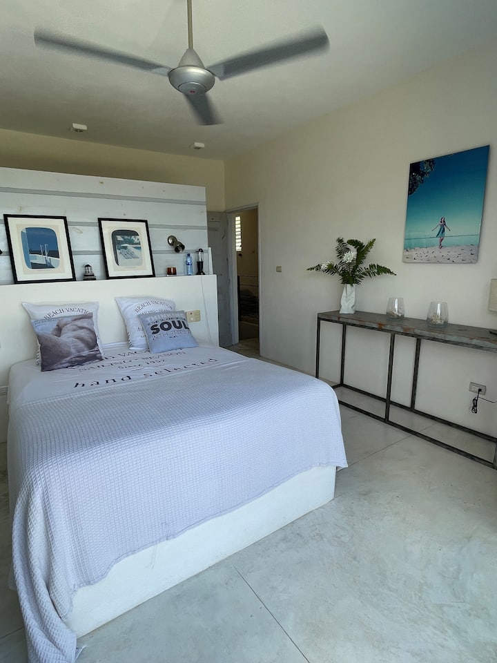 Hoofdslaapkamer 2 met uitzicht op het eigen terras, met uitzicht op natuur en zee. Queensize bed met kleedkamer, badkamer en en-suite toilet.  De plafondventilator en de zijluik openen naar de natuur, garanderen permanente ventilatie.