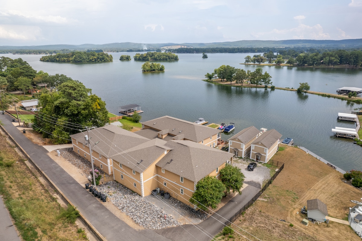An aerial view showcases the well-designed condo complex alongside serene Lake Hamilton. The image captures the surrounding lush greenery, tranquil water, and private boat slips, highlighting the peaceful setting and scenic landscape that enhances the lakeside experience.