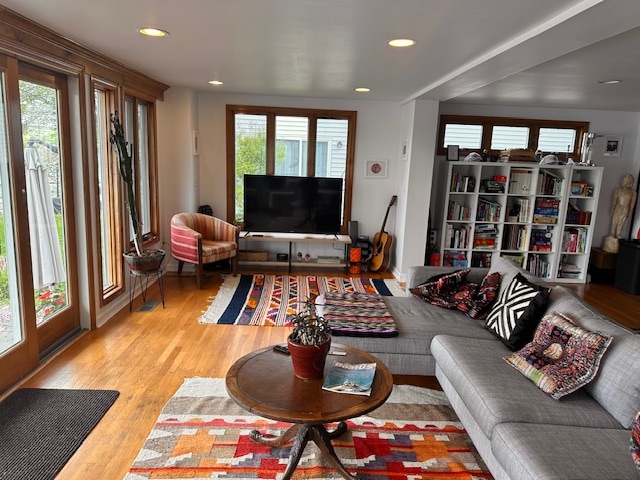 A welcoming living area is highlighted by large windows allowing natural light to fill the space. A sectional sofa and a circular coffee table are complemented by vibrant rugs. A television and bookshelves enhance the room's functionality, with a cozy seating area nearby.