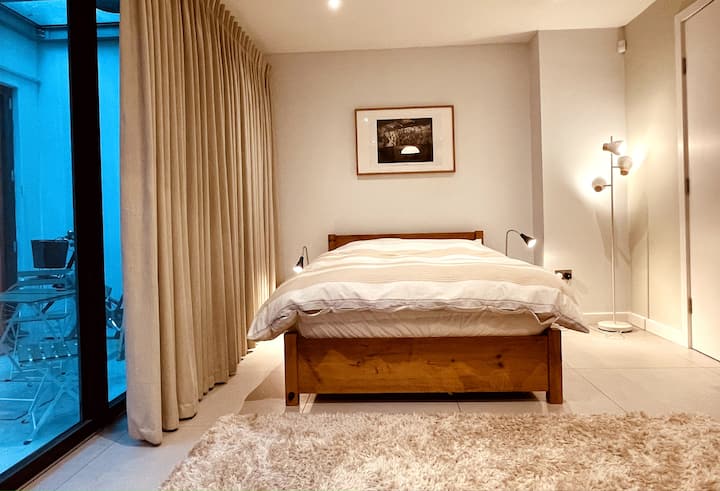 Chumba cha kulala mara mbili kilicho na kabati la nguo lililojengwa ndani. Kwenye sakafu ya chini ya ghorofa. Madirisha ya sakafu hadi dari na milango ya kioo iliyokunjwa imefunguliwa hadi mwanga mpana wa 2,50, milango ya ukubwa wa juu na dari za urefu wa mita 3 hufanya isionekane kama chumba cha chini ya ardhi. 