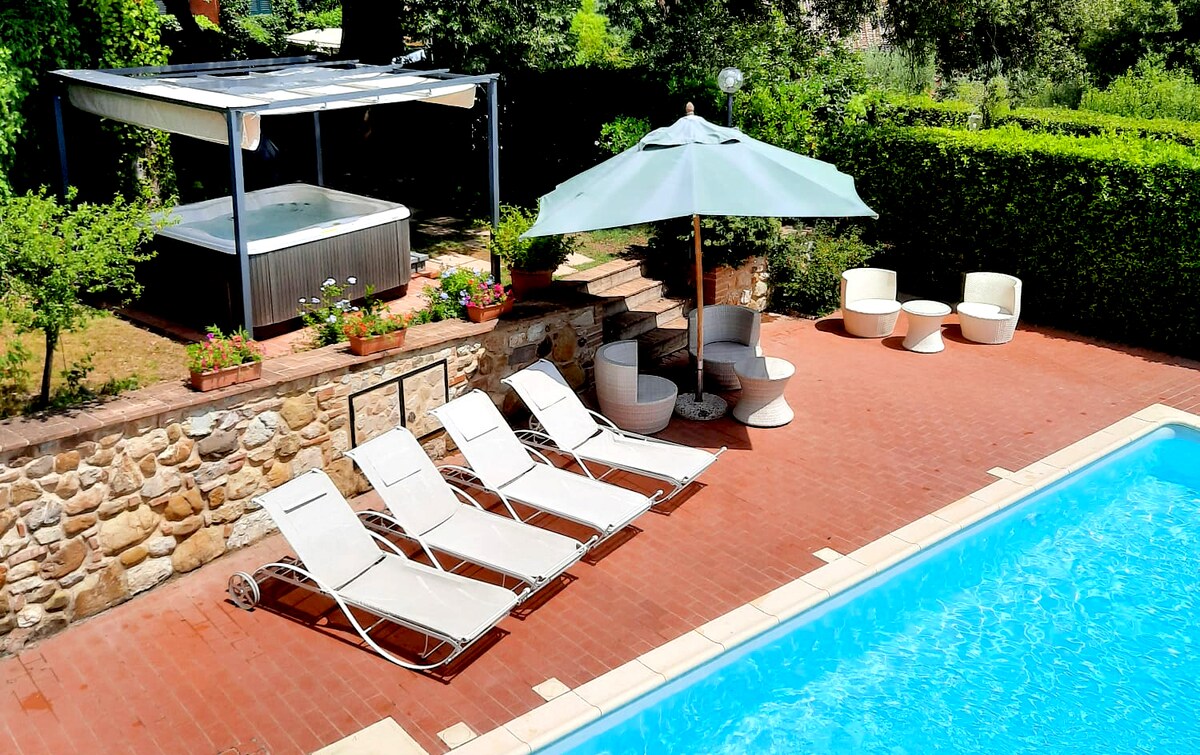A private garden area features a swimming pool surrounded by multiple lounge chairs. A hot tub is situated under a canopy, with a large umbrella providing shade. Stone steps lead to a landscaped area, enhancing the inviting outdoor space.