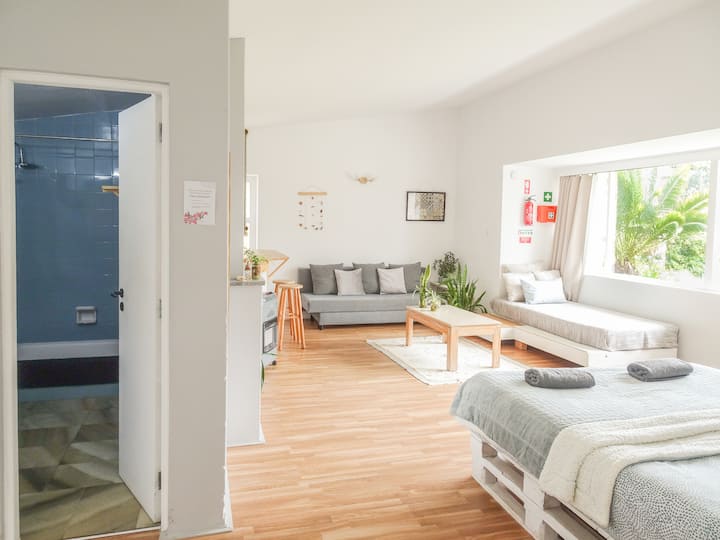 Videira Studio, a bright and spacious studio adjacent to the main villa. Enjoy a comfy king bed, cozy corner with two couches which can be converted to single beds, a private bathroom, and kitchenette. Panoramic windows frame stunning garden views.