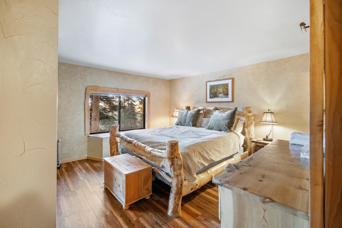 The master bedroom features a king bed in matching Aspen log furniture, an oversized window, and hardwood floors, enhancing the clean, open feel of this mountain retreat.
