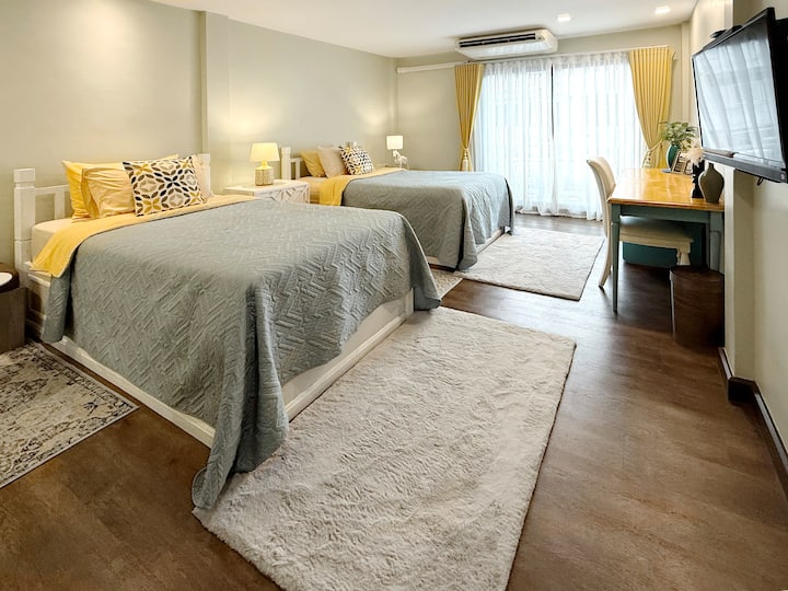 Cozy, modern twin-bed room perfect for friends or family. Enjoy soft lighting, fresh colors, and two plush rugs. Features include a dedicated work desk and flat-screen TV. A restful, stylish space designed for a comfortable stay