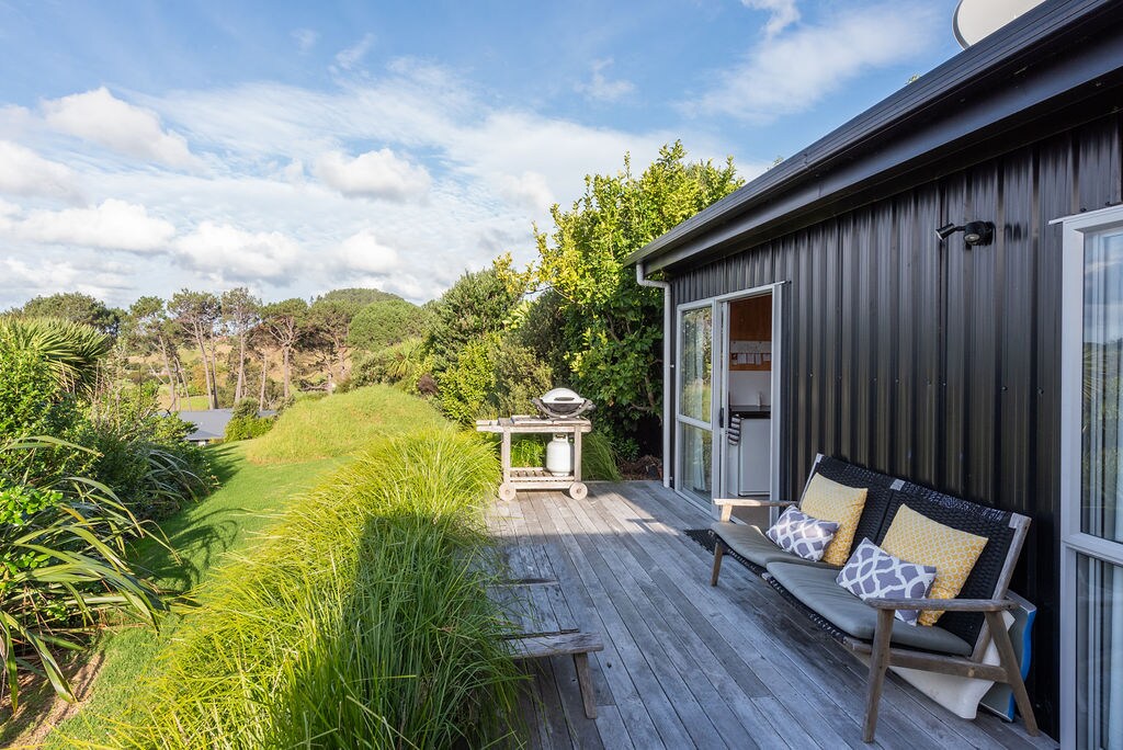 A private deck area features comfortable seating and a Webber BBQ, surrounded by lush greenery and expansive views of the landscape. Large sliding doors provide access to the cozy indoor space, inviting natural light into the inviting cabin.