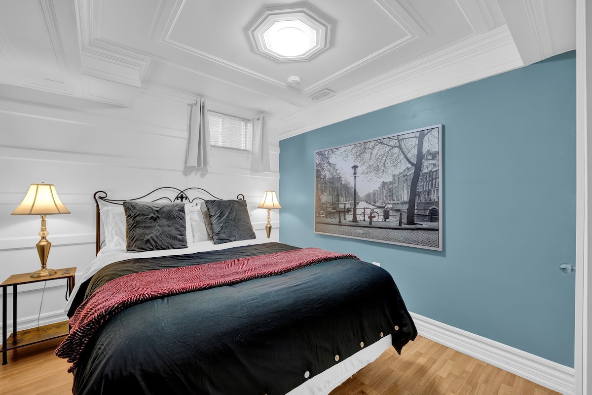 De slaapkamer met een pluche queensize bed met veel daglicht en verduisterende gordijnen voor privacy.  Je geniet van het gemak van doordachte details zoals nachtlampjes, oplaadstations en een volledige spiegel. 