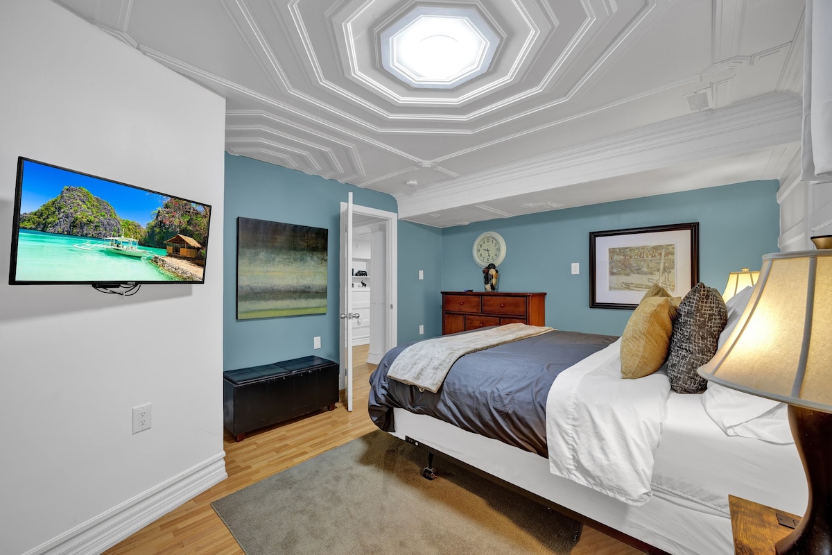 De slaapkamer met een pluche queensize bed met veel daglicht en verduisterende gordijnen voor privacy.  Je geniet van het gemak van doordachte details zoals nachtlampjes, oplaadstations en een volledige spiegel. 