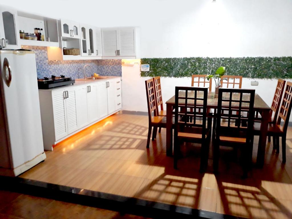 The kitchen area features a spacious dining table with six chairs, illuminated by soft lighting. A modern refrigerator and gas stove are included, along with white cabinetry and a blue tiled backsplash. A decorative green wall adorns the background, enhancing the clean look.