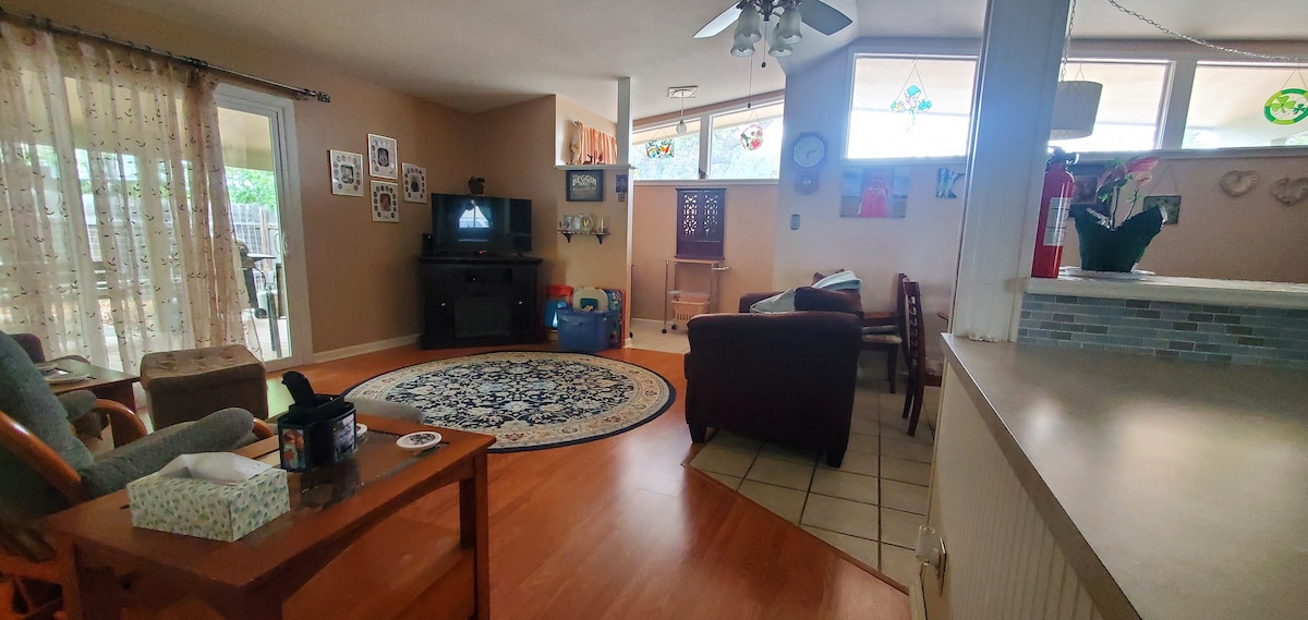 A comfortable living area is highlighted by a patterned area rug and a television. Natural light enters through multiple windows, illuminating the space. A covered patio can be seen through the sliding doors, and various decorative artwork adorns the walls.