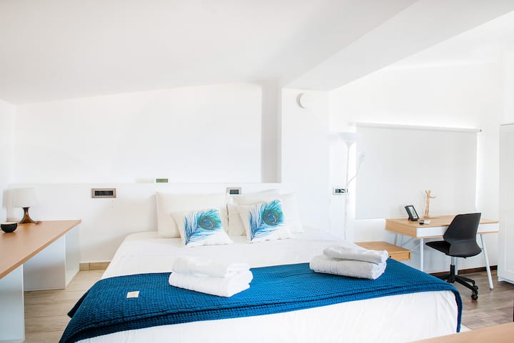 Tercer dormitorio de estilo loft con una cómoda cama doble, sábanas blancas y un práctico escritorio en la esquina, bañado en luz natural: un espacio luminoso y relajante para dormir o ponerse al día con el trabajo.