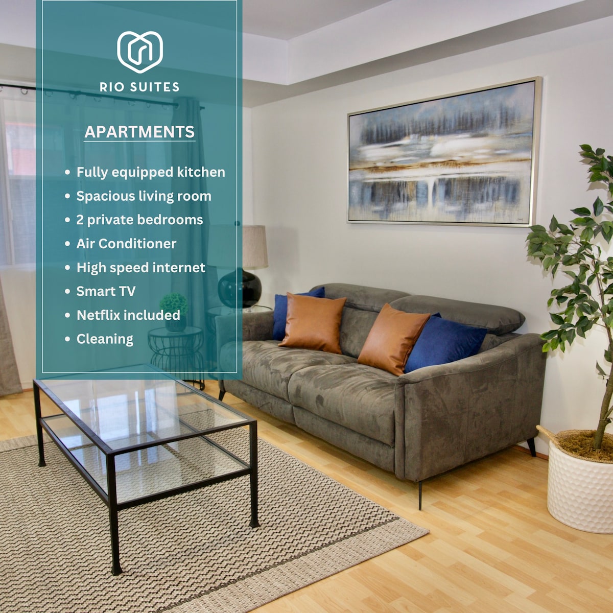 A well-lit living room is presented, featuring a comfortable gray sofa adorned with decorative pillows. A glass coffee table is positioned in front of the sofa, with an area rug underneath. A large piece of abstract artwork is displayed on the wall, adding visual interest.