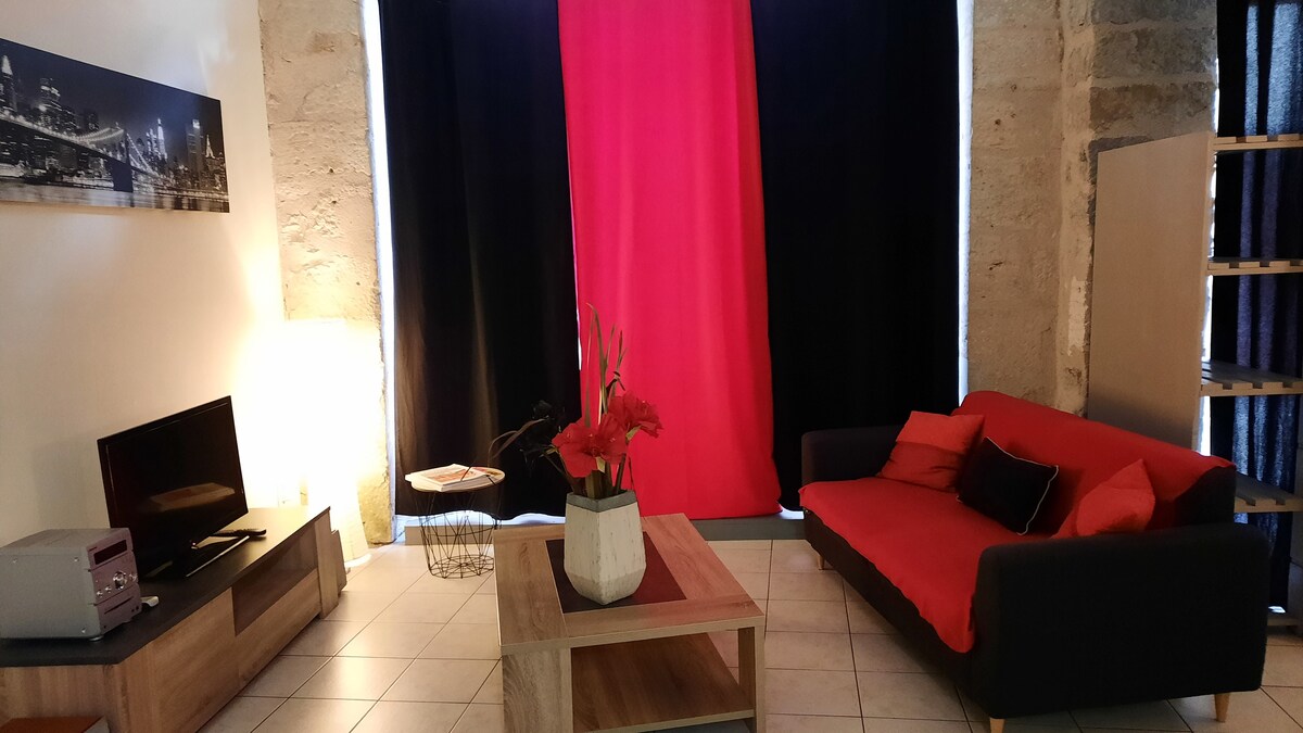 The living area features a cozy non-convertible sofa adorned with cushions and a coffee table. A television is positioned on a wooden unit, complemented by a bright pink curtain and dark drapery, enhancing the room's ambiance.