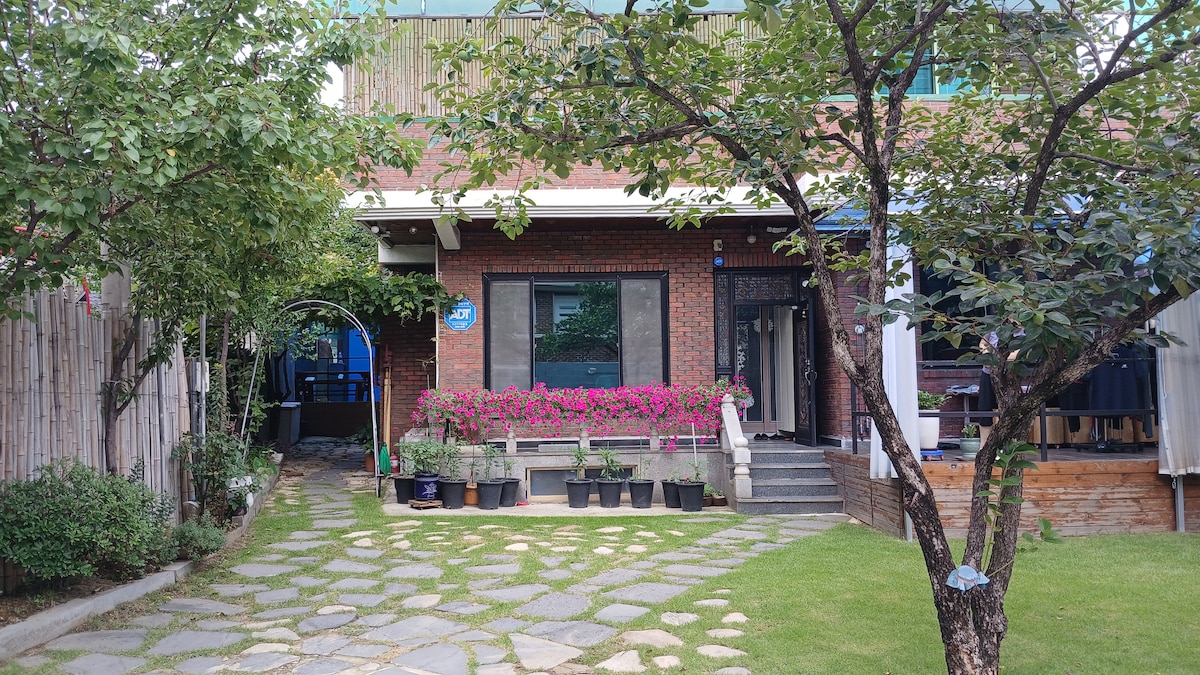 The exterior of the two-story home features a well-maintained garden with a charming stone pathway leading to the entrance. Colorful flower pots line the front, and lush greenery enhances the inviting atmosphere. A patio area is visible on the side, providing additional outdoor space.
