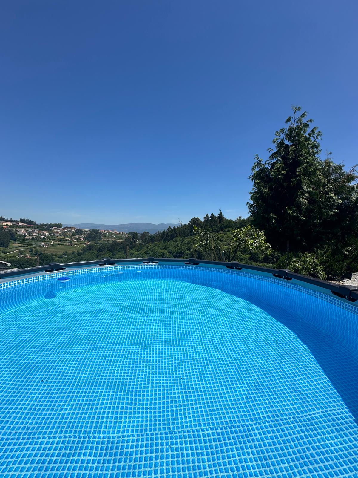 A private circular pool is surrounded by a clear blue water, reflecting the bright sky above. Scenic views of rolling hills and distant mountains are visible in the background, offering a serene outdoor space ideal for relaxation.