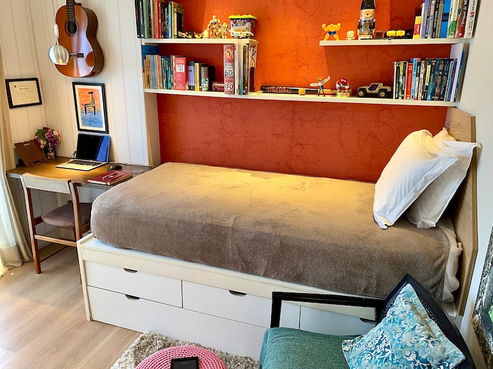 Cama macia, mesa iluminada e livros ao alcance. Um quarto feito para descansar com estilo e se inspirar com leveza · Soft bed, sunlit desk, and books within reach. Izba vytvorená na pokojné noci a inšpirované dni.