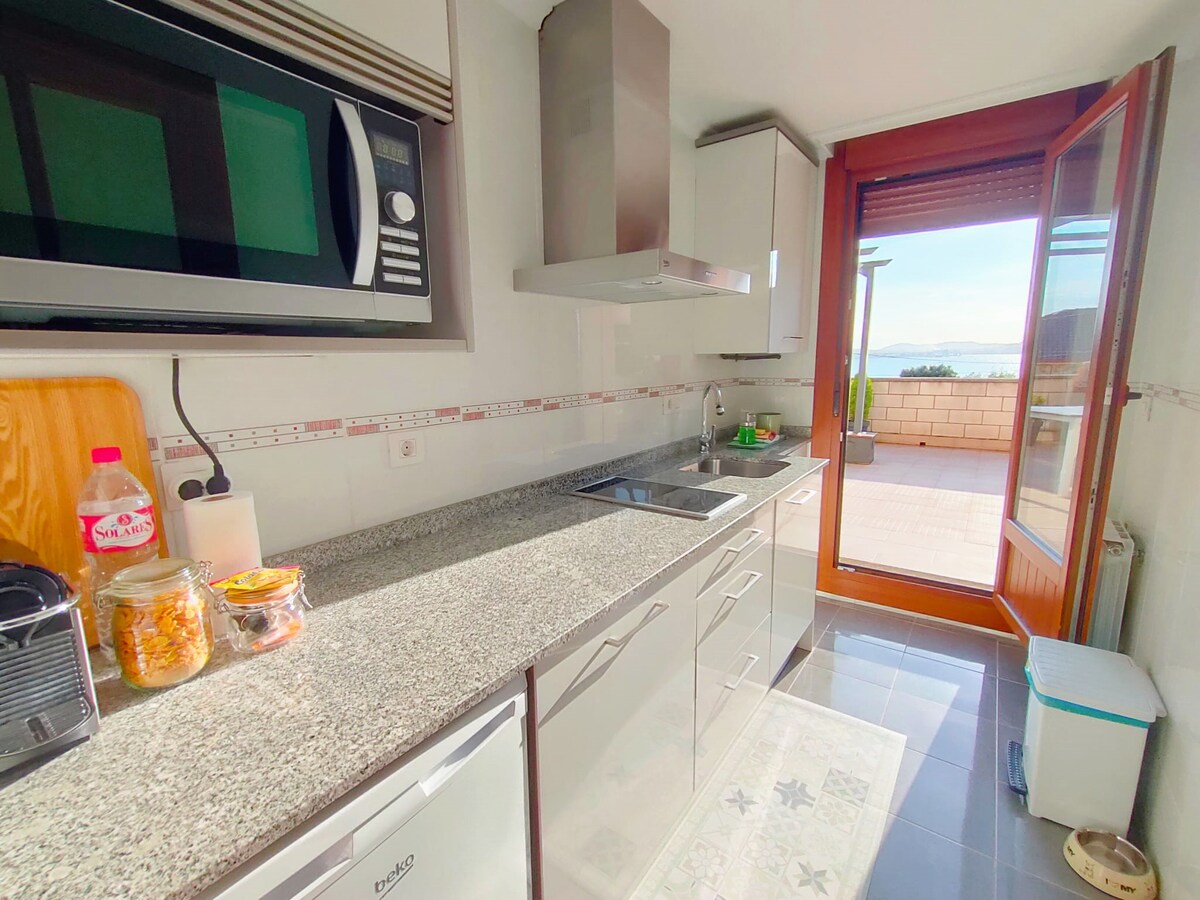 The kitchen features a modern design with granite countertops and a range of appliances, including a microwave and a stovetop. A window offers views of the outdoor terrace, allowing natural light to brighten the space. A door opens onto the terrace, extending the living area.