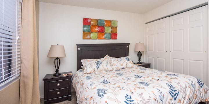 The bedroom features a comfortable queen-sized bed, blackout curtains on the window, nightstands, a dresser and a closet.