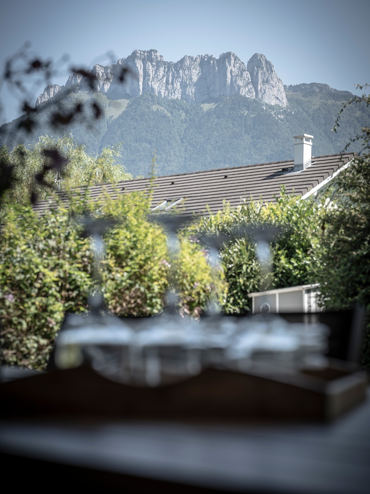 Distant mountains tower against a clear blue sky, creating a serene backdrop. In the foreground, greenery frames the view, adding a sense of tranquility. This peaceful environment highlights the natural beauty surrounding the accommodation.