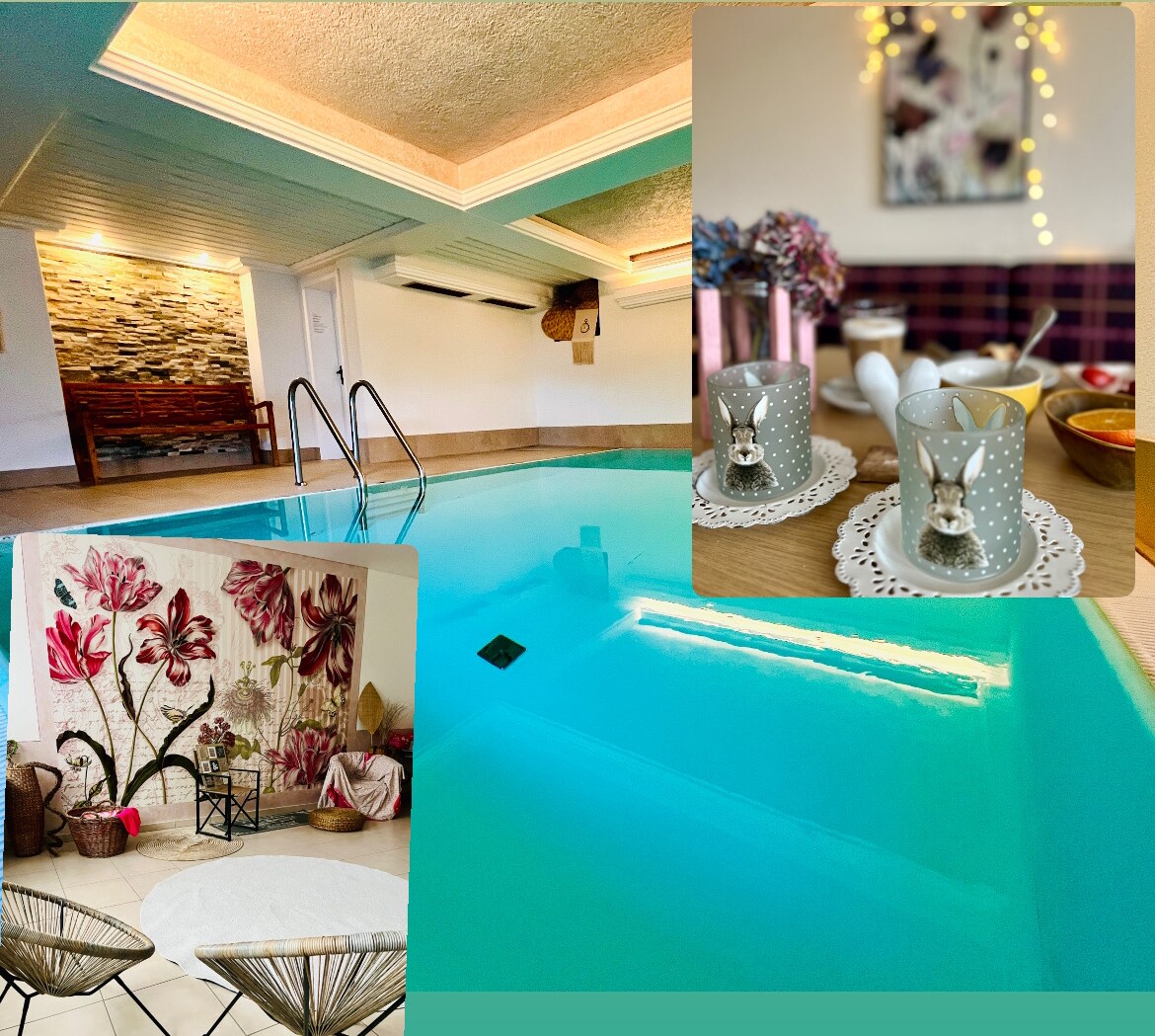 An indoor pool area is highlighted, featuring turquoise water reflecting soft overhead lighting. A seating area with decorative plants and vibrant floral artwork is visible, complemented by a table set with charming decorative glasses and an arrangement of dishes, creating an inviting atmosphere.